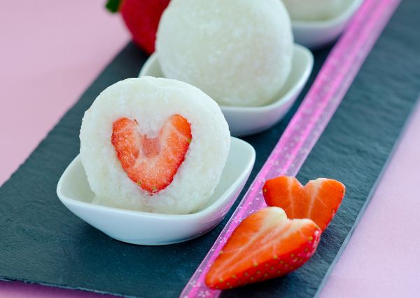 Strawberry sweets confectionery. Mochi dessert with strawberry heart in a white dish on a black slate board with pink ribbon.