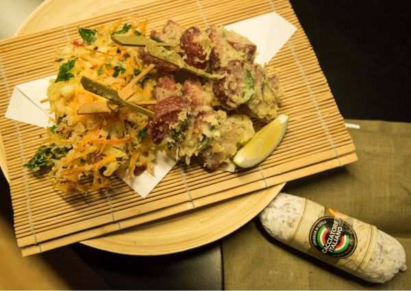Cacciatore Italiano Tempura. Fried Italian salami skewers with lemon wedge on bamboo mat.