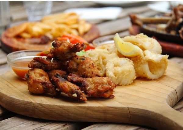 Fried food trends. Crispy fried chicken wings, calamari with lemon, and fries on a wooden board.