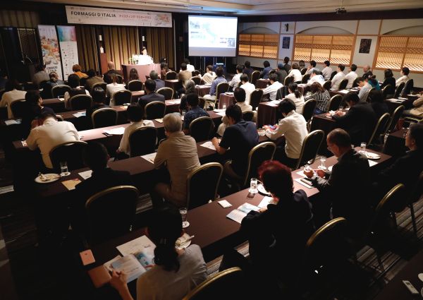 Audience at Japan Tastes Italian Cheeses event. Speaker on stage, projector screen. Italian cheese tasting masterclass.