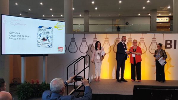 Italian Food Awards USA 2019: Pastiglie Leone wins award. People on stage with award, screen showing product.