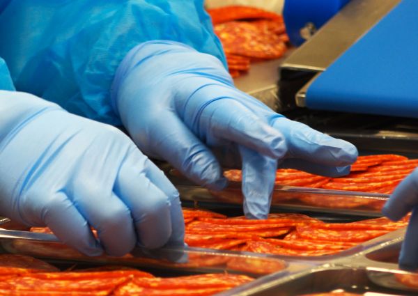 Veroni USA quality: Slicing Italian salami. Close-up of gloved hands preparing meat for packaging.