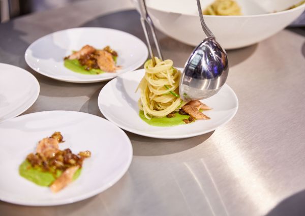 Barilla Master of Pasta dish. Spaghetti, salmon, and green sauce on a white plate. Ladle pouring pasta.