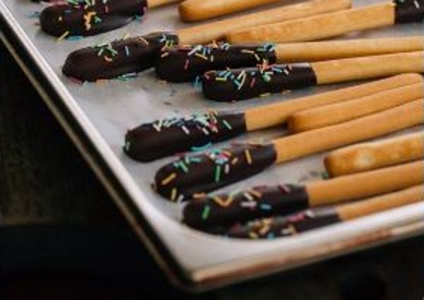 Chocolate-dipped breadsticks with sprinkles on a tray. Grissini dessert for Breadstick Day.