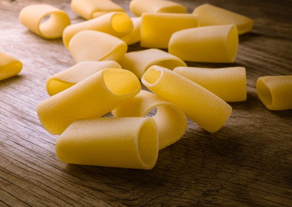 Paccheri pasta. Close-up of uncooked, large tube-shaped Italian pasta on a wooden surface.