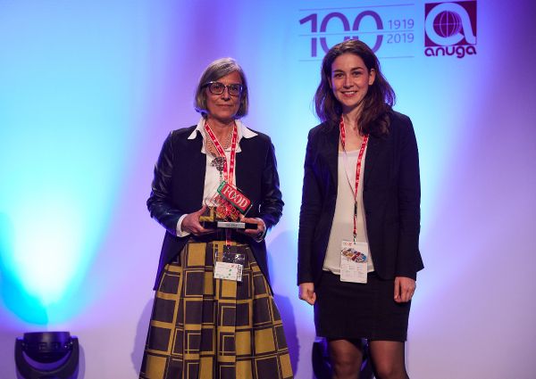 Two women at Italian Food Awards 2019. One holds an award. Anuga logo in background.