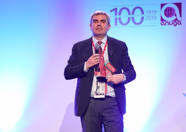 Italian Food Awards 2019 winner. Man holding microphone and award. Anuga logo in background.