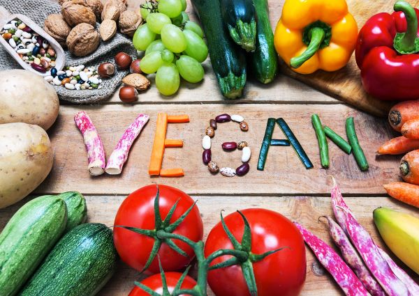 World Vegan Day: Fresh vegetables, nuts, and beans spell out Vegan on a wooden surface. Plant-based diet concept.