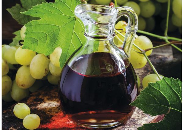 Piedmont specialties: Glass jug of red wine with green grapes and leaf.