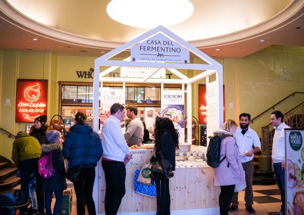 Italian dried fruit stand with Casa del Fermentino sign. People shop for fermented nuts at a Whole Foods Market.