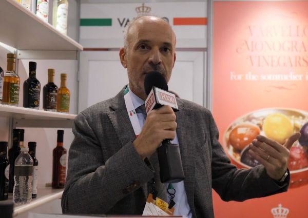 Varvello olive oil and vinegar maker speaking at a food expo. Italian products on display.