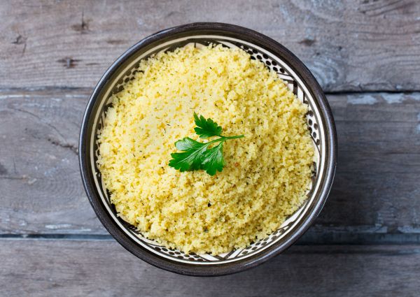 Italian couscous dish in bowl with parsley garnish on wooden table.