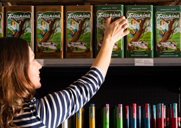 Woman selecting Toscantina Italian olive oil in tin cans at an Australian deli. European foods.