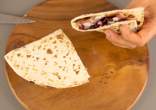Italian piadina flatbread with ham and vegetables on a wooden board. Fast casual food.