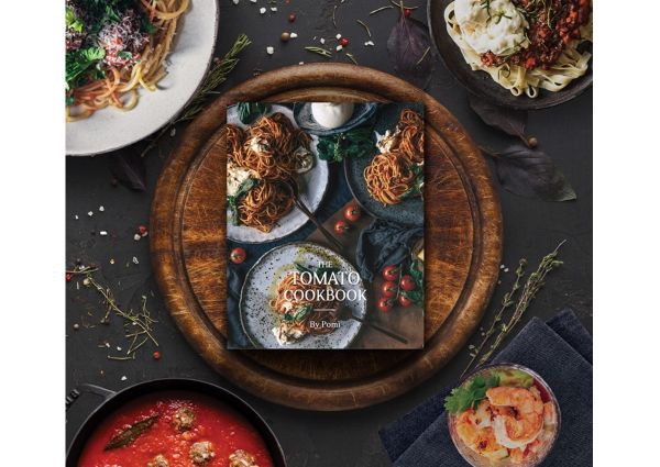 Pomì Tomato Cookbook on a wooden board surrounded by tomato-based dishes.