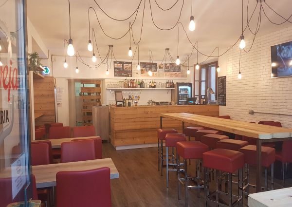 La Caveja restaurant interior. Romagna soul, world mind. Cozy dining with wood bar, red seating, and unique lighting.