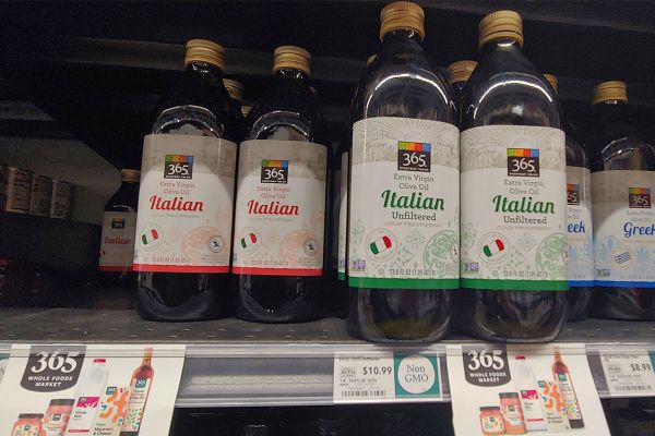 Bottles of 365 Italian extra virgin olive oil on a Whole Foods shelf.
