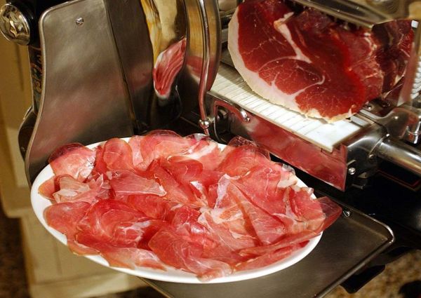 Culatello di Zibello PDO. Sliced cured meat on a plate, next to a meat slicer. Italian delicatessen.