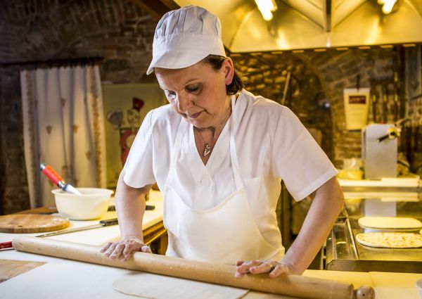 Woman making Piadina Romagnola PGI. Chef rolls out dough with a rolling pin. Traditional Italian flatbread.