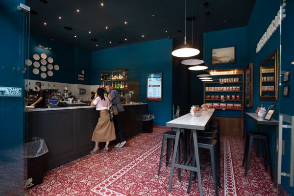 Caffè Napoli interior. Neapolitan espresso bar with seating, bar, and staff. Red patterned floor.