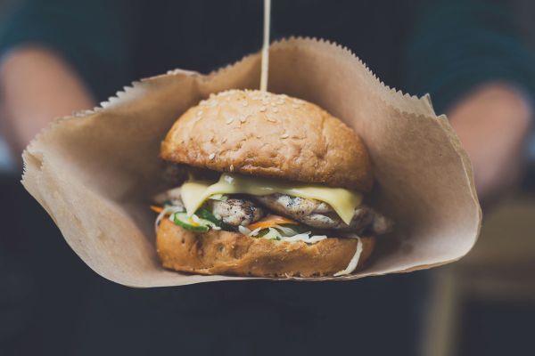 Veggie burger with cheese, cucumber and sesame bun in a paper bag. Hamburger Day food.