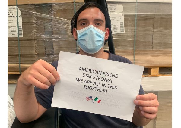 Pastificio Mediterranea worker holds Stay Strong sign for US clients. American & Italian flags. Food industry support.