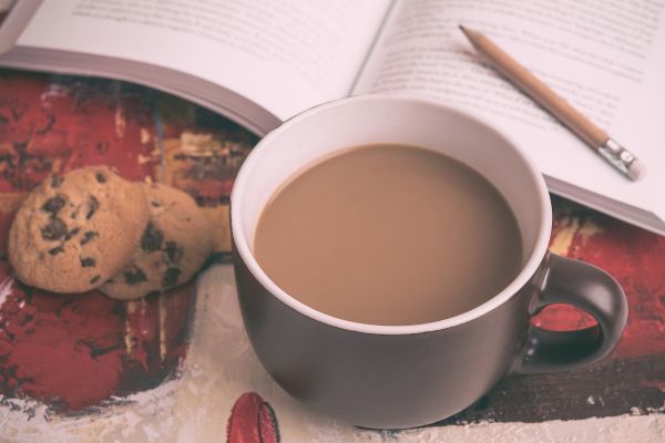 Chocolate Day treat: coffee mug, chocolate chip cookies, book, and pencil on a colorful surface.