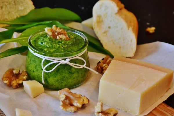 Barilla pesto in jar with cheese, bread, and walnuts. Fresh, vibrant green pesto.
