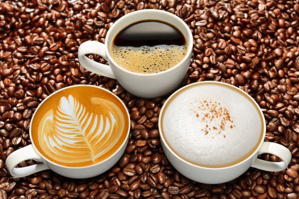 Three cups of Italian espresso, cappuccino, and latte art on coffee beans for International Coffee Day.