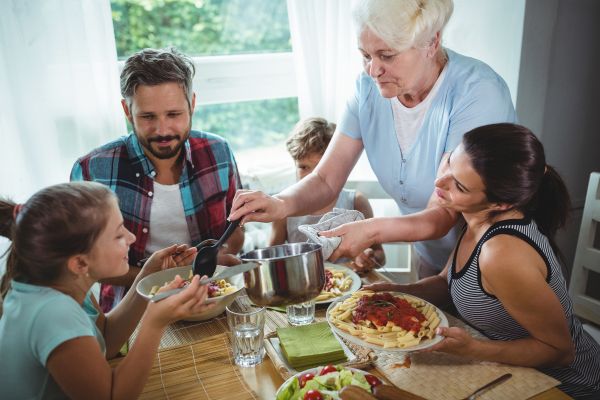 Family at table eating pasta for World Pasta Day. Grandmother serves Al Dente pasta to family. Italian food culture.
