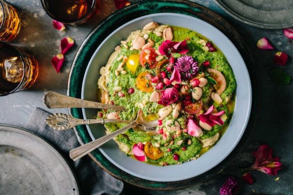 Whole Foods 2021 food trends: Hummus bowl with pesto, tomatoes, beans, nuts, pomegranate seeds, and edible flowers.
