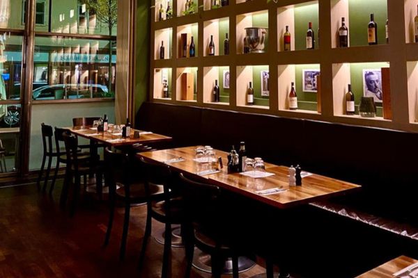 Restaurant interior with wood tables, chairs, and wine bottle display. Fine dining.