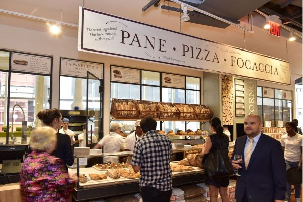Eataly Dallas bakery. Fresh pane, pizza, focaccia. Wood-burning oven. Shoppers browsing bread selection. Italian food market.