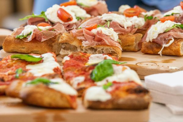 Eataly Dallas Italian food: Pizza and bruschetta with prosciutto, tomatoes, and mozzarella cheese on a wooden board.