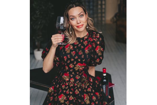 Woman holding glass of Chianti wine. Bottle of Riserva Chianti wine in view. Floral dress.