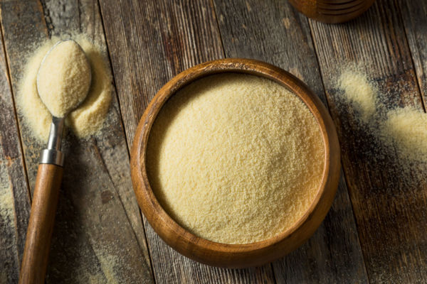 Organic semolina durum flour in wooden bowl with spoon on wood background.