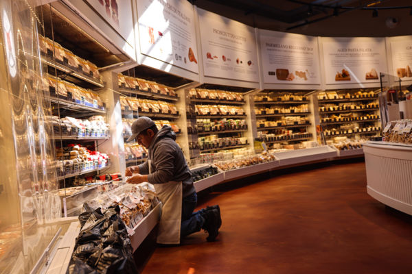 Eataly Italian food market. Worker stocking shelves with prosciutto, cheese, and other gourmet food products.