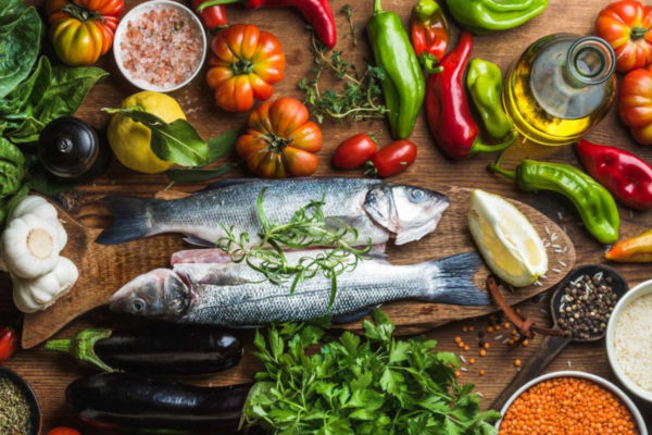 Mediterranean diet ingredients: fish, vegetables, olive oil, and spices on a wooden board.