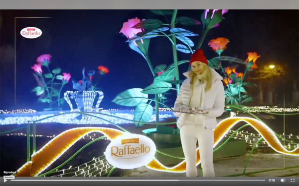 Ferrero Raffaello Rose Garden in Poland. Woman in white with Raffaello chocolates, illuminated rose decorations at night.
